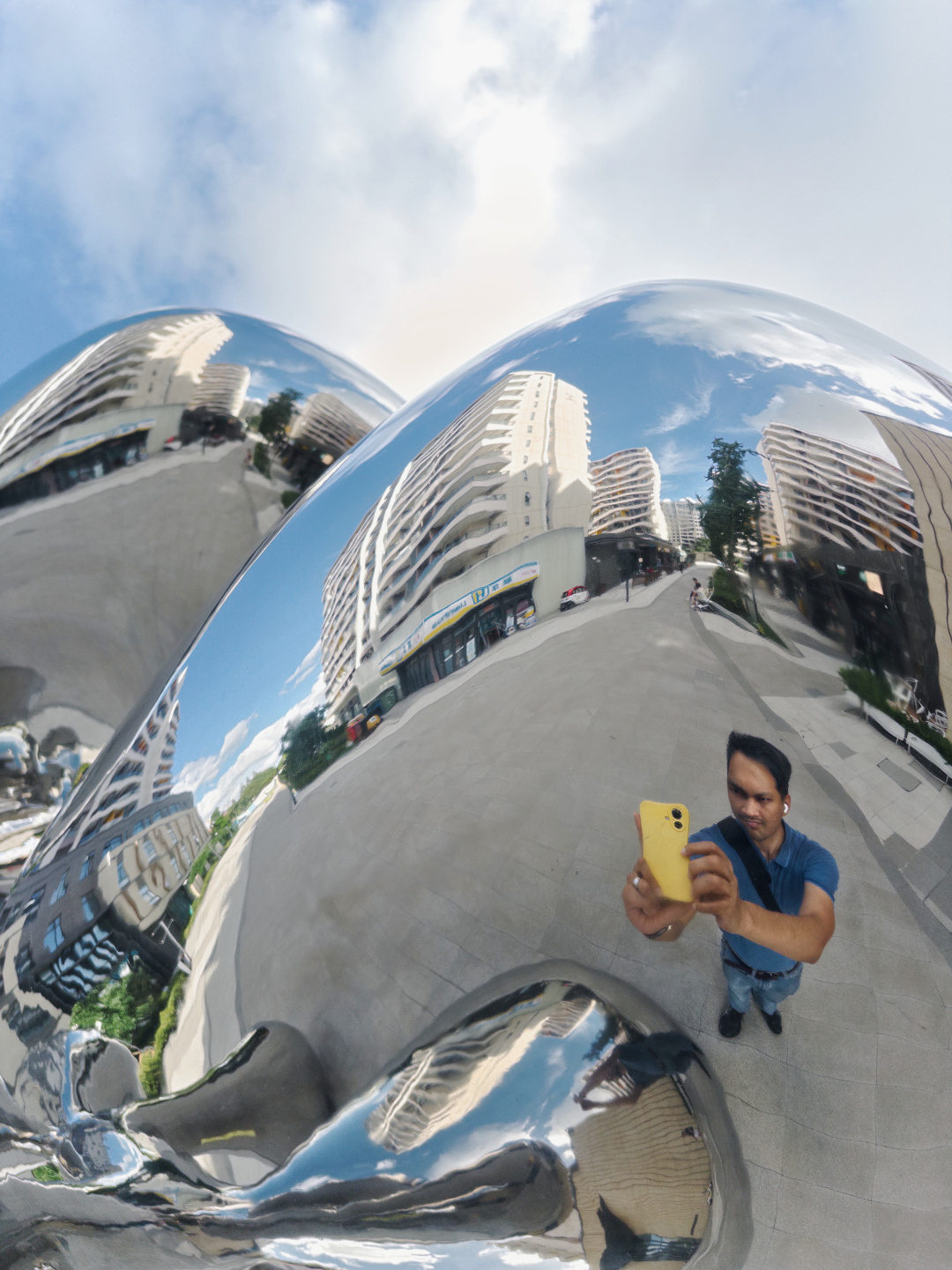 Photographer standing in a couryeard of an apartment complex reflected in a steel sculpture