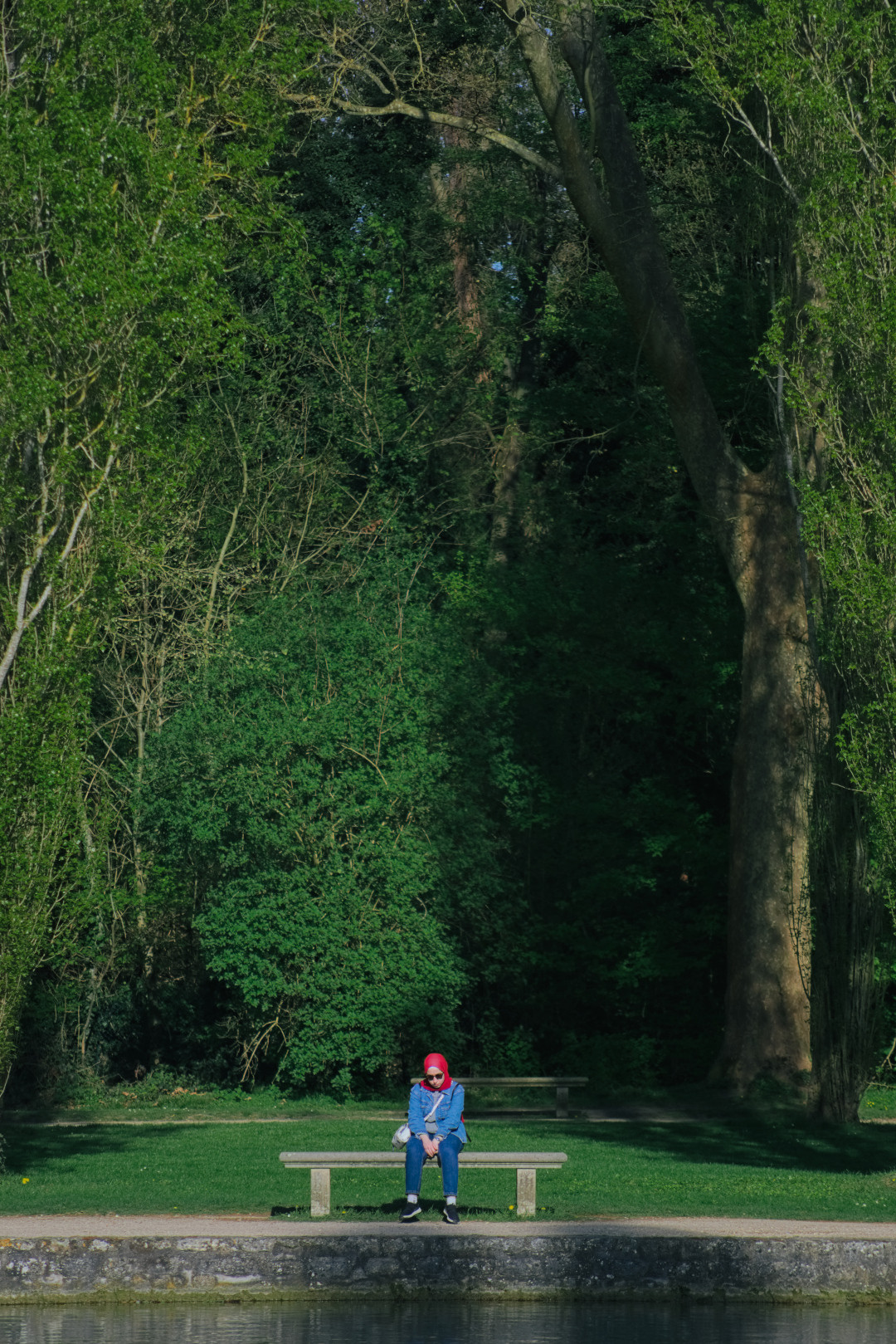 A woman in a red headscarf sitting on a bench among tall green trees